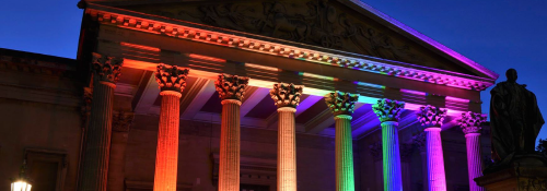 image of university building lit up in multiple colours. Used to advertise Pride campaign